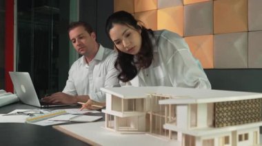 Bir grup mimar mühendis birlikte çalışıyor ve ofis tasarımı hakkında tartışıyorlar. Genç mühendis ev modelini ölçerken yönetici dizüstü bilgisayar kullanıyor. İş tasarımı konsepti. Yönlendirici.