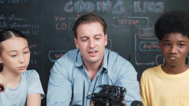 Akıllı öğretmen araba modelini farklı öğrencilere denetliyor. Melez ırk dinleyen liseli çocuklar masada dizüstü bilgisayarı ve kabloları olan robot model sistemini açıklıyor. Öğretim