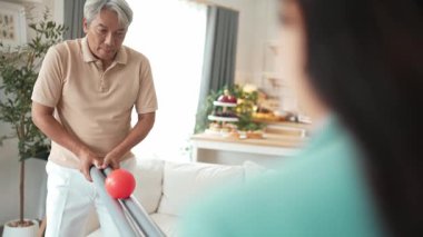 Yaşlı bir adam evde partneriyle top yuvarlama oyunu oynuyor, zihinsel ve fiziksel sağIık için el-göz koordinasyonu, odaklanma ve motor becerileri pratiği yapıyor. Sağlık hizmetleri konseptini engelliyor. Myrmidon.