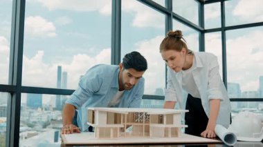 Profesyonel kooperatif iş arkadaşı ev modelini incelerken kalem kullanarak mimari modeli işaret eden yetenekli proje yöneticisi. Mimar mühendis takımı modeli belirlemek için birlikte çalışıyor. İzleme