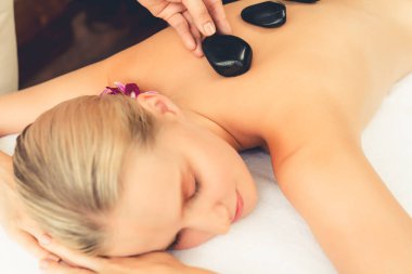 Lüks tatil köyündeki kaplıcalarda sıcak taş masajı. Gün ışığı sükunet ortamında, mutlu kadın müşteri bazalt taş masajından zevk alıyor. Rahatlatıcı bir sıcaklıkla vücudun üzerinde süzülüyor. Sessiz.