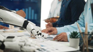 Bir robot ve insan takımı modern ofis ortamında stratejik karar verme mekanizması için veri ve grafikleri analiz ederek çalışmanın geleceğini gözler önüne seriyor.