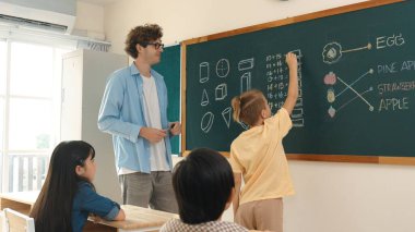 Akıllı çocuk tahtada dururken matematik teorisine cevap yazıyor. Beyaz çocuk sınıfın önünde sınav yaparken çekici erkek öğretmen ilköğretim sınıfına bakıyor. Eğitim. Pedagoji.
