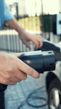 İlerici işadamı, şehir merkezinde dolaşmadan önce şarj cihazından elektrikli arabasına şarj prizi takıyor. Çevre dostu şarj edilebilir araba, sürdürülebilir ve temiz enerjiyle çalışıyor..