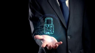 Bir işadamı, veri güvenliğini sembolize eden, karanlık bir arkaplanda teknoloji unsurlarını barındıran sanal bir kilit sunarak hassas bilginin korunmasının önemini vurguluyor. Dörtgen