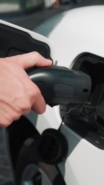İlerici işadamı, şehir merkezinde dolaşmadan önce şarj cihazının fişini şarj istasyonundan elektrikli arabasına çekiyor. Çevre dostu şarj edilebilir araba, sürdürülebilir ve temiz enerjiyle çalışıyor..