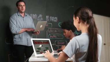 Afrikalı erkek manken tamir ederken beyaz kız programlama ya da kodlama sistemi. Öğretmen elinde dizüstü bilgisayar tutarken çeşitli çocukların web geliştirme programı yazmalarına bakıyor. Yenilik eğitimi. Öğretim