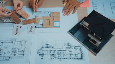Tasarım analizi için masaya dizilmiş planlar ve ölçekli bir modelle mimari planlamayla uğraşan çeşitli profesyonelleri gösteren işbirlikçi bir sahne. SACTR
