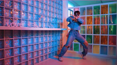 Gece kulübünde kameraya bakarken güneş gözlüklü Asyalı dansçı serbest dans ediyor. Mutlu sokak dansçısı dans ediyor ve renkli parlak neon ışığı ya da yol gösteren ışıkla ayak seslerini gösteriyor. Mutluluk.