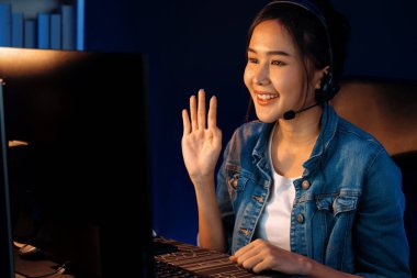 Sunucu kanalı Asyalı etkileyicisi canlı yayında konuşuyor. Sosyal medyada kulaklık takıyor, bilgisayar kaydı yapıyor, dinleyicileri selamlıyor ve Neon Modern Stüdyoları 'nda online olarak koçluk yapıyor. Taktik.