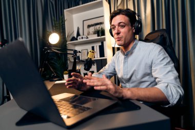 Sunucu kanalı akıllı yayıncı laptopta canlı sosyal medya uygulaması arıyor, kulaklık takıyor ve modern ofis stüdyosundaki mikrofonu kullanıyor. Bireysel.
