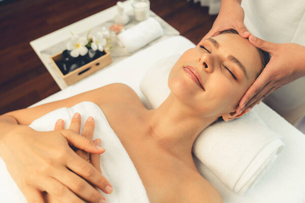 Caucasian woman enjoying relaxing anti-stress head massage and pampering facial beauty skin recreation leisure in dayspa modern light ambient at luxury resort or hotel spa salon. Quiescent