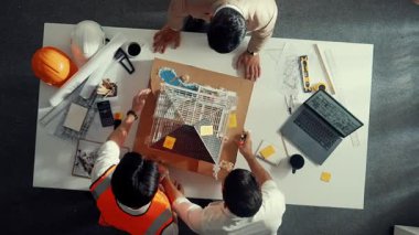 Mimar 'ın yapışkan notlar yazıp ev modeline yerleştirdiği yukarıdan aşağıya hava görüntüsü. Profesyonel proje yöneticisi toplantı masasında dizüstü bilgisayar ve ekipmanlarla bina inşaatını denetliyor. Hizalama.