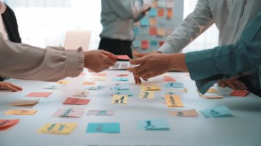 Çeşitli bireyler canlı bir beyin fırtınası oturumunda, iyi aydınlatılmış bir ofiste renkli yapışkan notlar hakkında fikir alışverişinde bulunarak, işbirlikçi ruhu ve yenilikçi düşünceyi somutlaştırıyorlar. SACTR