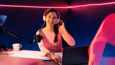 Geceleri podcast 'te olumlu konuşmalar yapan, pembe neon ışıklı modern stüdyoda sunum için dizüstü bilgisayar kullanan, gülümseyen, genç, güzel Asyalı bir etkileyiciydi. Taktik.