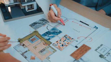 Mimari bir kat planı için el ele tutuşmalar. Renkli kumaşlar ve detaylı çizimler modern bir çalışma alanında yaratıcı tasarım süreçleri sergiliyor. SACTR