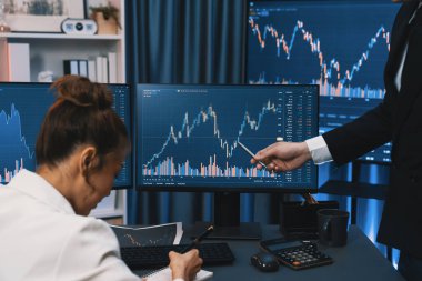 PC ekranlarında dinamik borsa istatistiklerini tartışan iş ortaklarının kağıt üzerinde not alması, para birimi grafiğindeki yüksek ya da düşük nokta ile gece neon çağındaki modern ofis karşılaştırıldığında. İnfobahn.