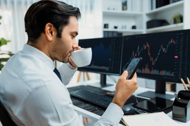 Elinde telefon dinamiğine odaklanan kahve fincanı tutan borsa yatırım ekranı veri analizini karşılaştırarak iç işlerinde yüksek kârlı finans teknolojisi pazarına yatırım yapıyor. Tahmin et..