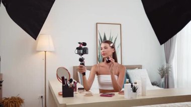 Sosyal medya için güzellik ve kozmetik video içeriği hazırlayan genç bir kadın. Güzellik blogcusu kameraya gülümserken seyircilere ve takipçilere güzellik bakımını gösteriyor. Düzenle