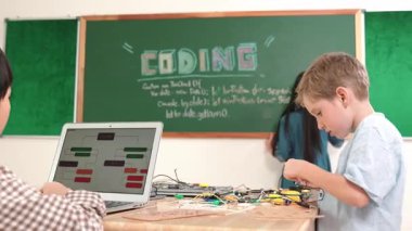 Kafkas arkadaşı STEM sınıfında elektrik panosunu tamir ederken Asyalı çocuk kodlama programı. Enerjik öğrenci kodlama mühendisliği komut yazarken ve yapay zeka yazılımını programlarken tahtada duruyor. Pedagoji.