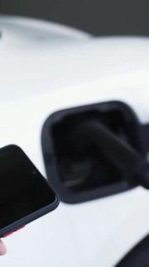 Akıllı telefon ekranı akıllı EV mobil uygulama üzerinde pil durumu EV araba garajdaki ev şarj istasyonu ile elektrik şarj ederken. Geleceğin yenilikçi EV arabası ve enerji sürdürülebilirliği. İnceleyin