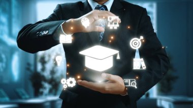 Bir işadamı, yenilik, öğrenme ve mesleki gelişimi sembolize ederek, modern ofis ortamında çeşitli eğitim sembolleri ve simgeler sergiliyor. Dörtgen