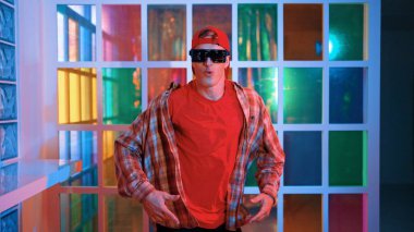 Komik break dansçı kameraya bakarken hiphop 'a doğru serbest adım atıyor. Çılgın mutlu hipster dans edip sokak dansı yaparken Led ışığında günlük kıyafet ve güneş gözlüğü takıyor. Mutluluk.