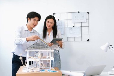 Güzel, genç, beyaz bir proje yöneticisi Asyalı mühendise, mühendislik masasında ev modelini ölçerken tablet kullanarak bina detaylarını anlattı. Tertemiz.