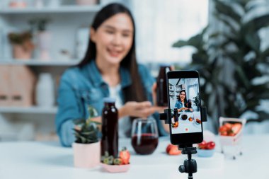 Seçici odaklı akıllı telefon ve gülümseyen genç, güzel Asyalı karışık çilek ve kiraz suyu detoksu değerlendirmesi sosyal medyada sağlıklı ürün tanıtımı sunuyor. Taktik.