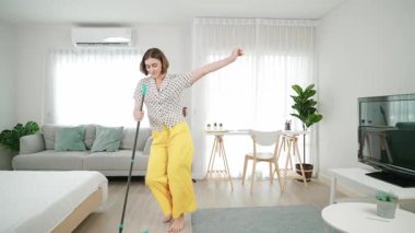 Modern apartman dairesinde dans ederken yerleri paspaslayan beyaz bir hizmetçi. Mutlu enerjik anne ya da temizlikçi müzik eşliğinde oturma odasını temizlemekten zevk alır. Yaşam tarzı. Pedagoji.