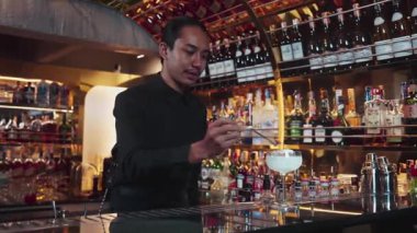 Asyalı barmen karışık kremalı votka bardağı servis ediyor. Önünde buzlu pembe çiçekli şeker, önünde özel içecek, lüks tezgah barında alkolü canlandırıyor. Vinosity.