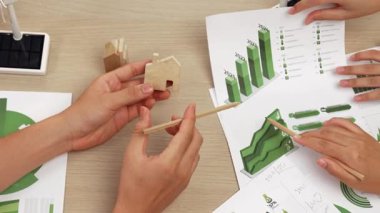 Mükemmel iş adamları, karbon ayak izini azaltmak, Dünya 'yı kurtarmak için grafik, yel değirmeni, ev ve ağaç modelini kullanarak yeşil enerjili eko ev projesinde işbirliği yaparlar. Eline odaklan. Tanımlama.