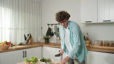 Mutlu baba yemek pişirirken müziğe geçiyor ve modern mutfakta öğle yemeği hazırlıyor. Aktif baba, sebze ve mutfak gereçleri ile çevrili sağlıklı yemek ya da salata yaparken şarkıyla dans ediyor. Pedagoji.