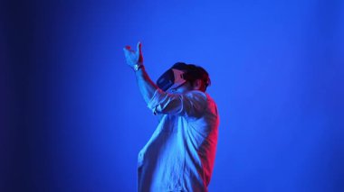 VR gözlüklü oyuncu sanal dünyaya girerken silah tutuşu yapıyor ve atış oyunu oynuyor. Mavi arka planda dururken simülasyon dünyasında zırh tutan yetenekli bir adam. Aygıt.