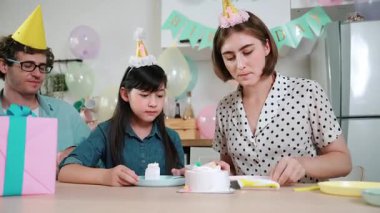 Kafkasyalı anne doğum günü pastasını kesiyor ve babaya verirken tatlıyı ayırıyor. Mutlu aile, kızının doğum gününde masada otururken parti şapkası takar. Özel durum konsepti. Pedagoji.