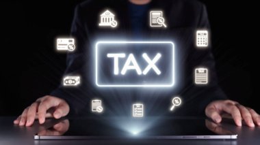 Bir işadamı, finans ve muhasebe stratejilerini sembolize eden dijital araçlar ve grafiklerle etkileşime geçerek, çağdaş bir ofiste yenilikçi vergi kavramları keşfediyor. Dörtgen