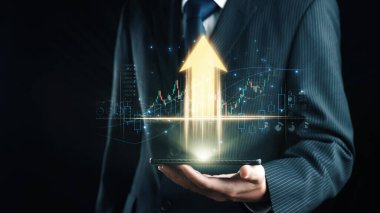 Takım elbiseli bir işadamı, parlak bir büyüme oku ve finansal veri grafikleri gösteren, başarıyı ve modern iş inovasyonunu simgeleyen bir akıllı telefon tutuyor. Dörtgen