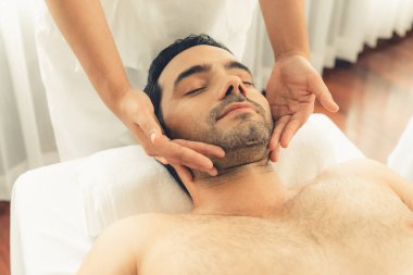 Beyaz adam stres önleyici kafa masajından ve lüks bir tatil beldesi veya otel spa salonundaki modern ışık ortamında yüz güzelliği eğlencelerini şımartmaktan hoşlanıyor. Sessiz.