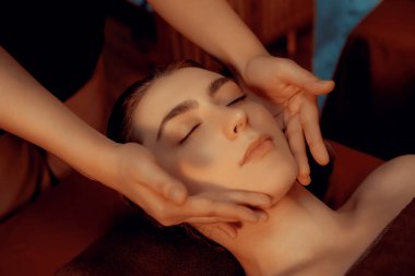 Beyaz kadın stres önleyici kafa masajı yapmaktan ve lüks otel veya otelde sıcak mum ışığında yüz güzelliği eğlencesi yapmaktan zevk alıyor. Sessiz.