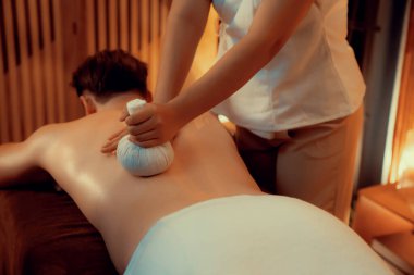 Sıcak bitkisel top spa masaj vücut tedavisi, masör erkek vücuduna nazikçe şifalı bitki torbası bastırıyor. Aromaterapi tesisinin sakinliği ve dinginliği kaplıca salonundaki mumların sıcacık ışığında. Sessiz.