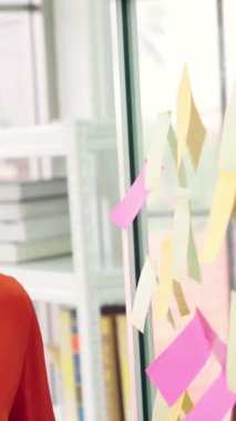İş adamları ofisteki proje planlama kurulunda çalışıyor ve proje gelişimini analiz etmek için iş arkadaşlarıyla sohbet ediyorlar. Düzenli olması için cam duvara yapıştırılmış yapışkan notlar kullanıyorlar. .