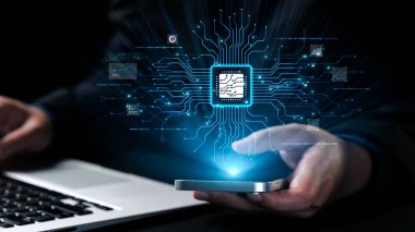 Bir kişi elinde parlak bir mikroçip grafiğini gösteren bir akıllı telefon tutuyor, arka planda bir dizüstü bilgisayarla ileri teknoloji ve yeniliği sembolize ediyor. Dörtgen