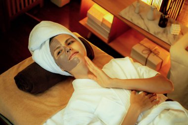 Kaplıca salonunun sakin atmosferi, üst düzey kadın müşteri sıcak mum ışığında kömür kömürü yüz kremi masajıyla kendini yenilemeye çalışıyor. Yüz bakımı ve güzellik konsepti. Sessiz.