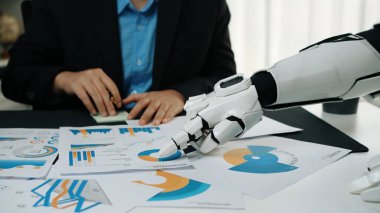 Bir robot el, bir masanın üzerindeki çizelge ve grafikleri analiz ediyor ve profesyonel bir ofiste teknolojinin ve insan işbirliğinin entegrasyonunu gösteriyor.