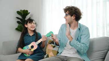 Mutlu bir babanın, ukulele çalan ve şarkı söyleyen akıllı kızına bakışının arkası. Mutlu baba motive oldu ve Amerikalı liseli kızı gitar çalmaktan zevk almaya teşvik etti. Aile eğlencesi. Pedagoji.