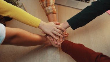 Çeşitli bireylerden oluşan bir grup, takım çalışmasını ve yenilikçiliğe odaklanmış ortak ofis ortamındaki desteği sembolize eden birleşik bir jest ile el ele veriyor. SACTR