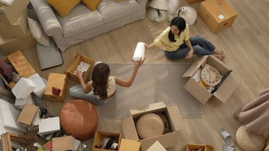 Oturma odasındaki mobilyaların taşınmasına yardım ederken yerde oturan mutlu oda arkadaşı. Yeni eve taşınmak için birlikte çalışan Asyalı lezbiyen aşığının havadan görünüşü. Yer değiştirme konsepti. Myrmidon.