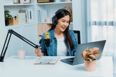 Sosyal medyada kulaklıkla canlı yayın yapan Asyalı sunucu modern stüdyoda yaşam koçluğu veya pazarlama dinleyicilerini selamlıyor. Taktik.