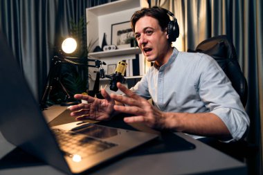 Sunucu kanalı akıllı yayıncı laptopta canlı sosyal medya uygulaması arıyor, kulaklık takıyor ve modern ofis stüdyosundaki mikrofonu kullanıyor. Bireysel.