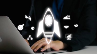 Bilgisayarda çalışan bir iş adamını gösteren parlak bir görüntü, dijital ortamda yenilik, başarı ve büyümeyi temsil eden bir roket sembolü ile birlikte. Dörtgen